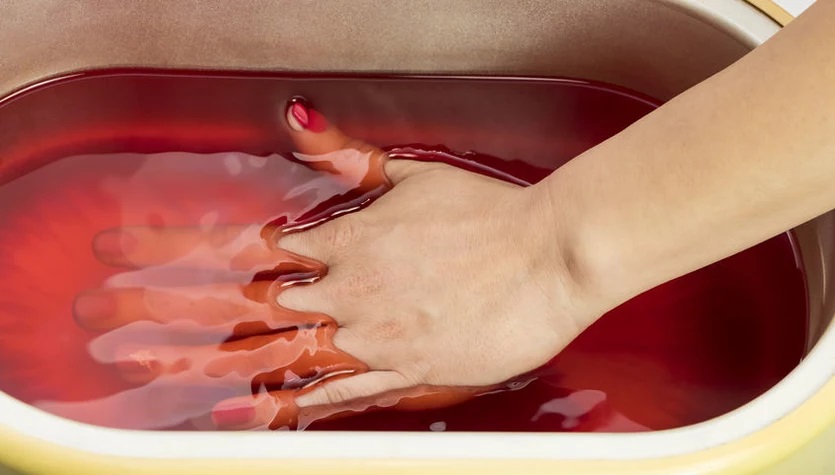 dłoń zanurzona w pojemniku z płynną parafiną w kolorze pomarńczowym