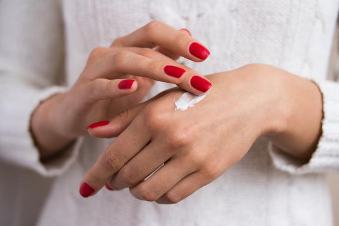 kobieta w białym swetrze pokazuje dłonie i rozsmarowuje biały krem na jednej z nich