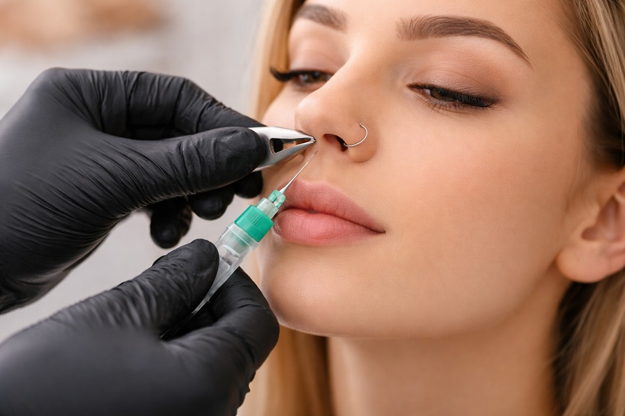 Piercing nosa wykonywany przez specjalistę – moment przekłuwania skrzydełka nosa sterylnym wenflonem w profesjonalnym gabinecie piercingu.