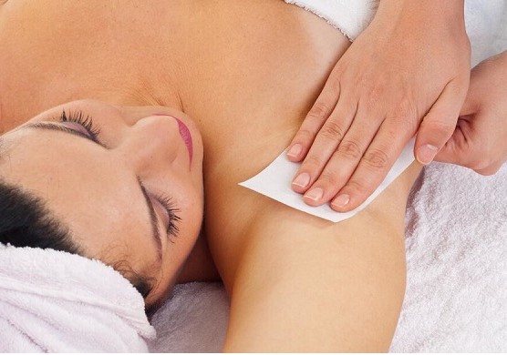 leżaca kobieta z ręcznikiem na głowie z pachy której usuwany jest wosk białym paskiem