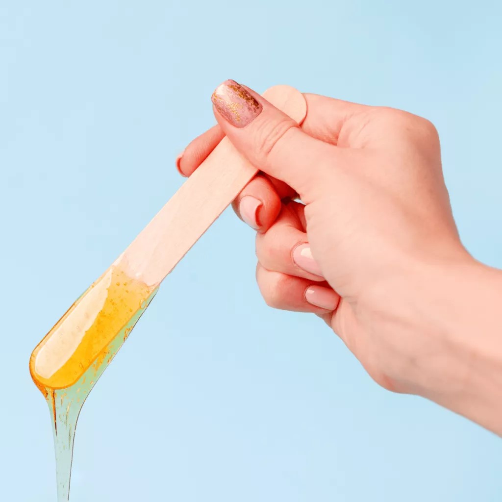 zdjęcie przedstawia kobiecą dłoń trzymającą szpatułke z której obcieka rozgrzany wosk